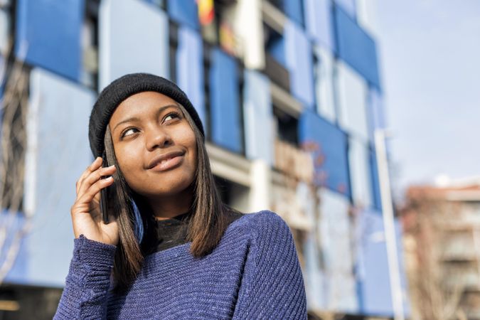 Female in wool hat and blue sweater chatting on cell phone and looking up