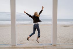 Joyful woman jumping raising hands up on wooden beach pier
