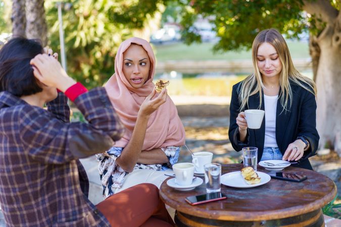Three women talking over coffee and baked goods on sunny outside table