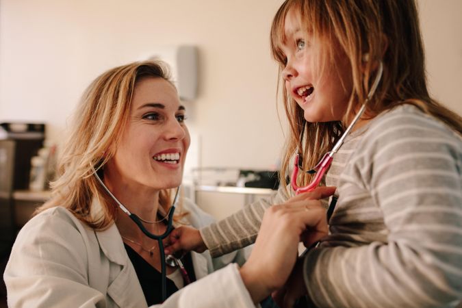 Friendly doctor and young girl examining each other with stethoscope