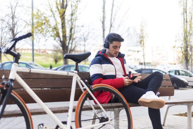 Young man with bicycle and using a smartphone while sitting on bench