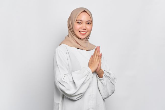 Smiling Muslim woman in headscarf and light blouse with hands together in prayer
