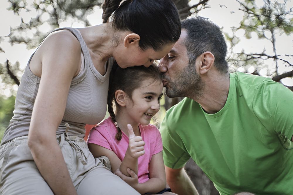 Loving family showing affection to happy daughter during forest walk bonding moment
