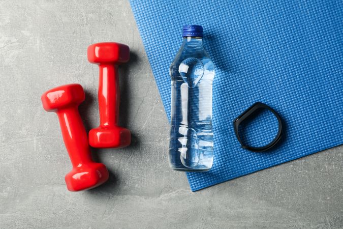 Looking down at clear water bottle with red weights on yoga mat