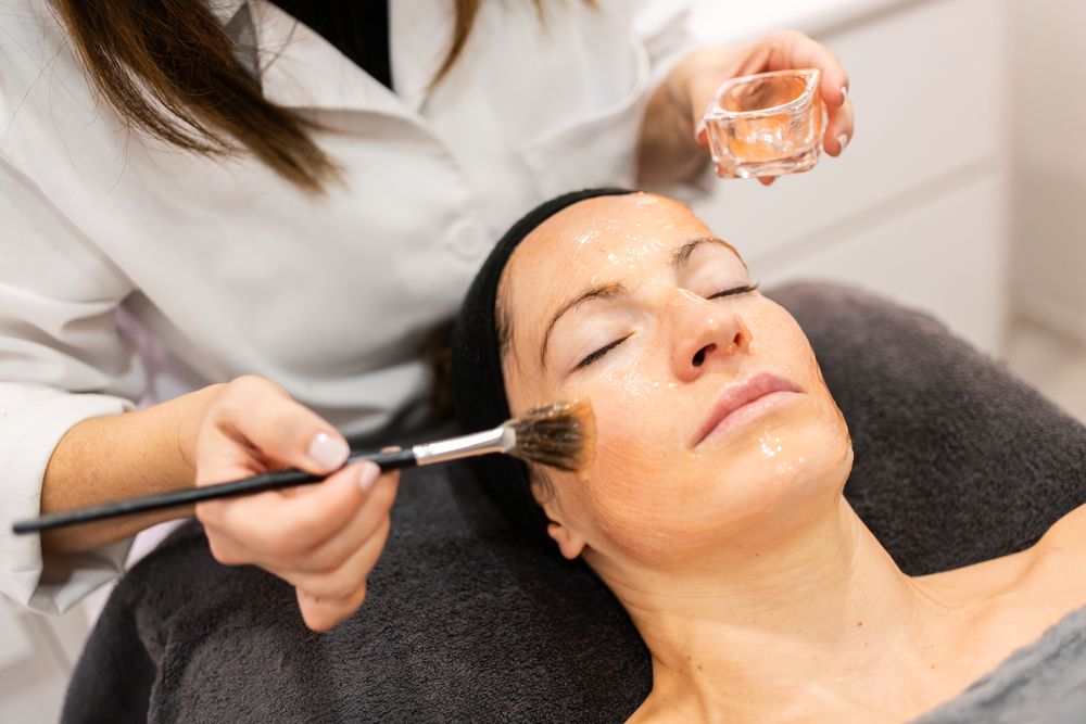Professional cosmetologist brushing product on client's forehead