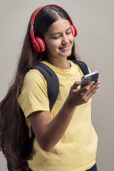 Smiling teenage girl with red headphones using smartphone and wearing yellow t-shirt and backpack