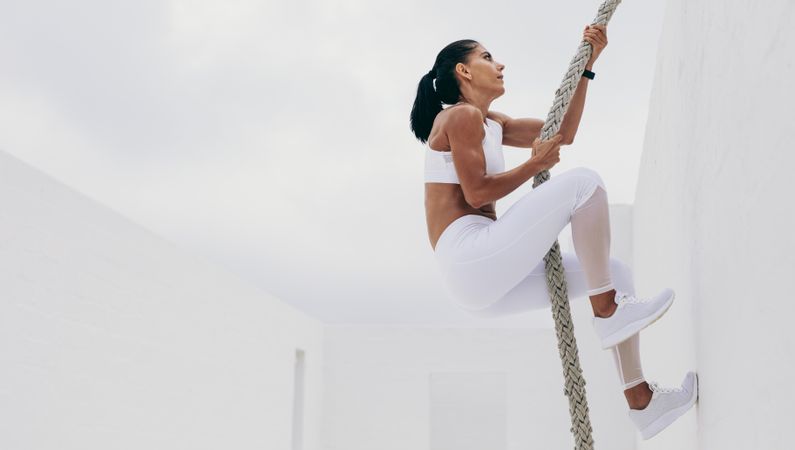 Athletic woman doing strength training climbing a wall using a rope