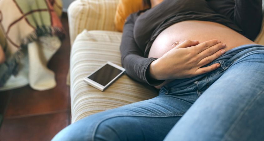 Pregnant woman lying on the couch caressing her belly