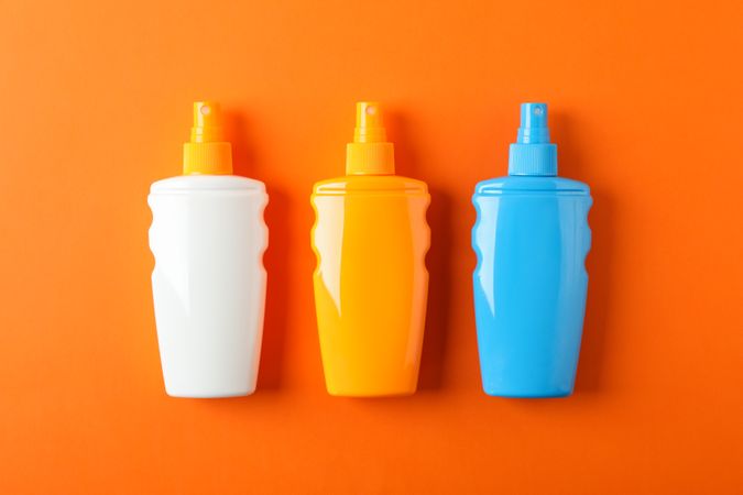 Flat lay composition with sunscreen sprays on color background. Space for text