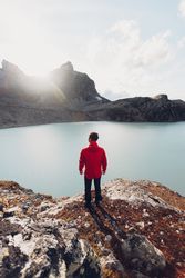 Back view of man in red jacket standing on waterside of frozen lake in Switzerland 4NJ6A4