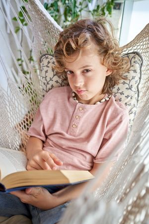 Boy with book lying in hammock and pouting lips