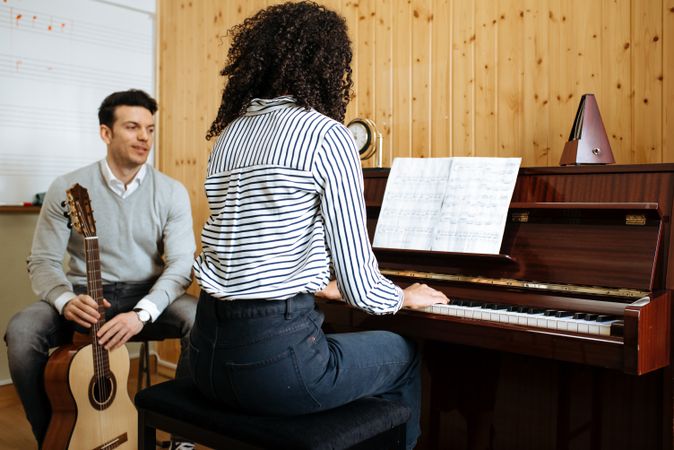 Woman playing piano near man playing guitar in studio