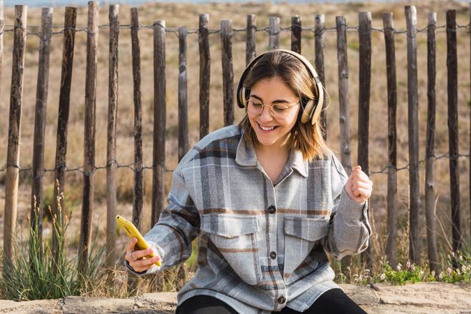Happy young woman using smartphone and listening to music in headphones in countryside