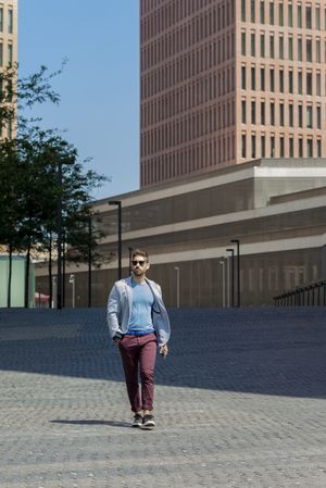 Young bearded man with sunglasses walking with hand on pocket