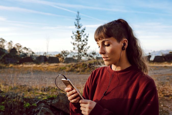 Young woman with piercing listening music on smartphone on hill