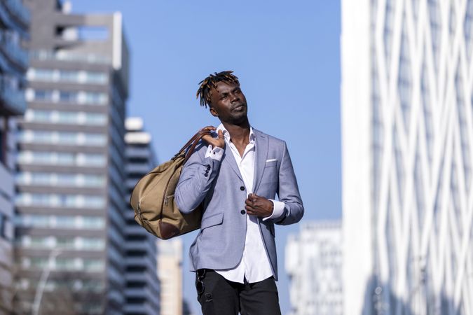 Black man wearing elegant suit standing in the street while looking in the distance on sunny day