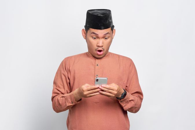 Muslim man in kufi hat surprised while looking down at smart phone