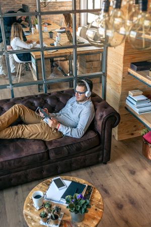 Man lying on an office sofa with tablet