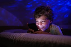 Delighted boy sending text message on cellphone at night
