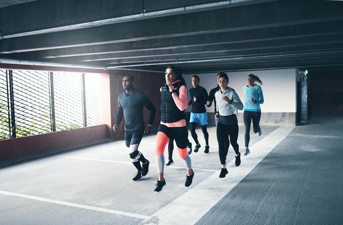 Multi-ethnic group of people in fitness gear running together in industrial concrete space