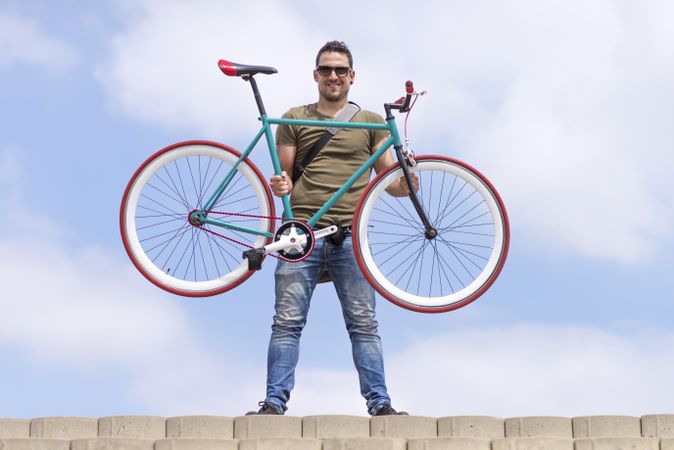Smiling male holding up bike with blue sky and clouds in background