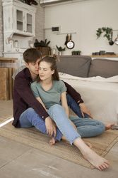 Relaxed couple hugging while sitting together on floor in living room