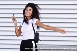 Arab woman in sport clothes with curly hair standing in front of wall with phone 0yBeO5