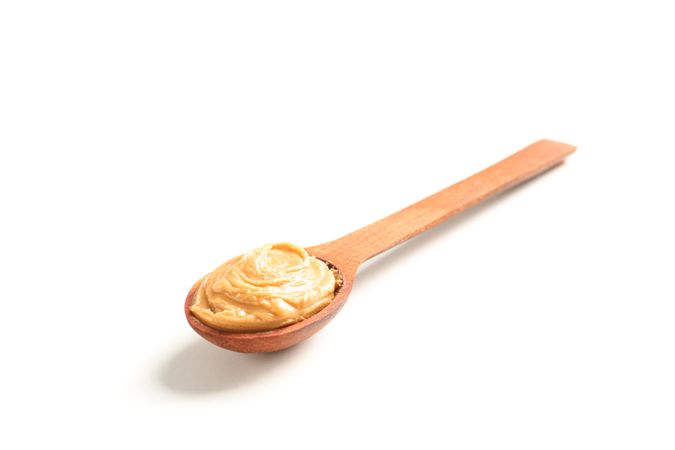 Creamy peanut butter in wooden spoon isolated on bright background. A traditional product of American cuisine