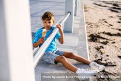 Boy eating an ice cream sitting near a seashore railing 5r9kvn