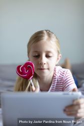 Young girl holding a pink heart shaped lollipop using a tablet 49mQ64