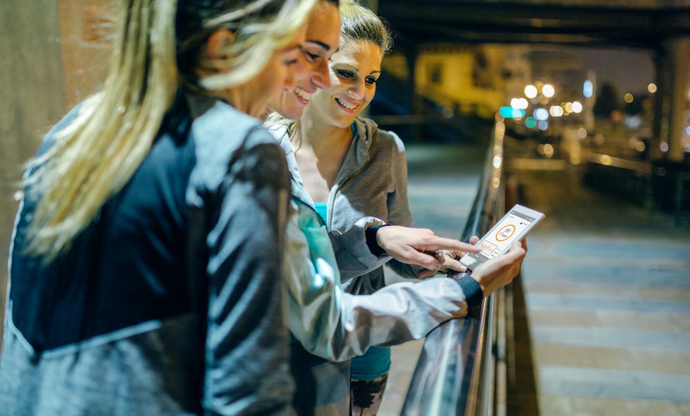 Smiling female runners friends checking activity summary on phone application