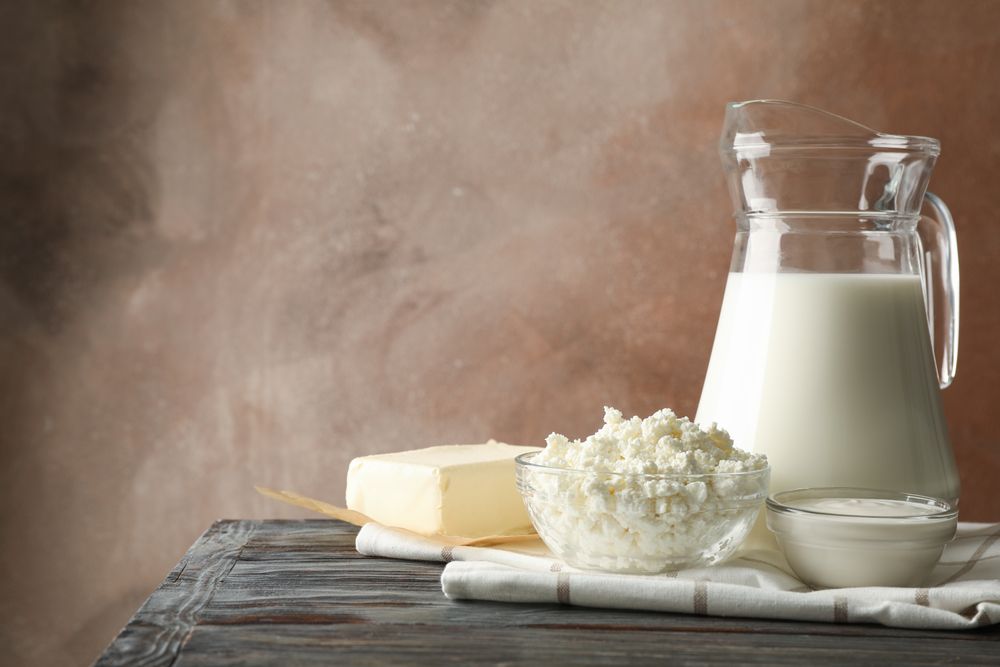 Milk, cottage cheese and butter on wooden table against brown background