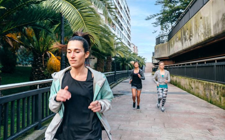 Brunette woman running ahead of female friends team on runway with palm trees