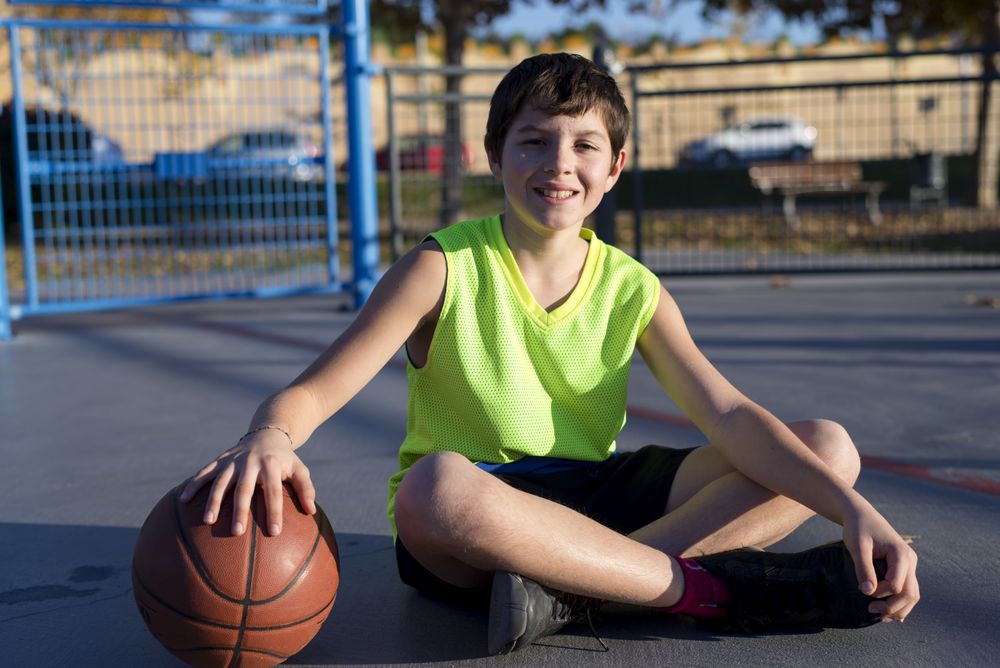 Young basketball player sitting on the court wearing a yellow sleeveless