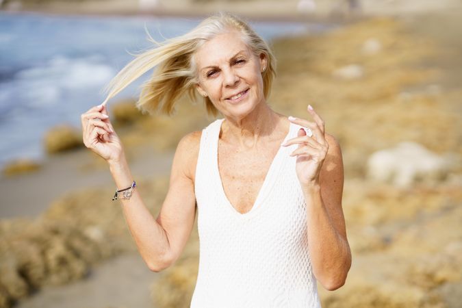 Older woman with grey hair moving hair off her face in the wind on the coast