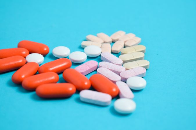 Variety of pIlls in heart shape on blue background with copy space