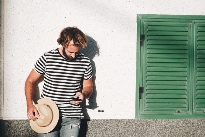 Young male leaning on wall with smartphone