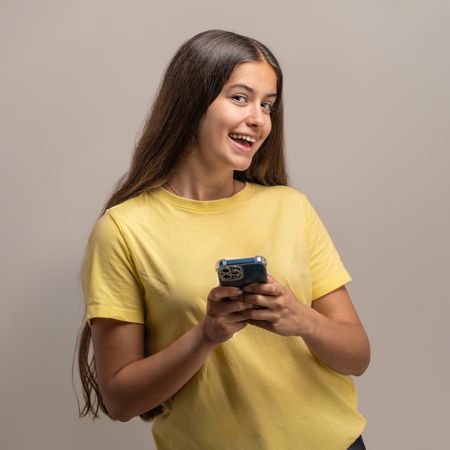 Cheerful young woman looks up from her smartphone while texting.