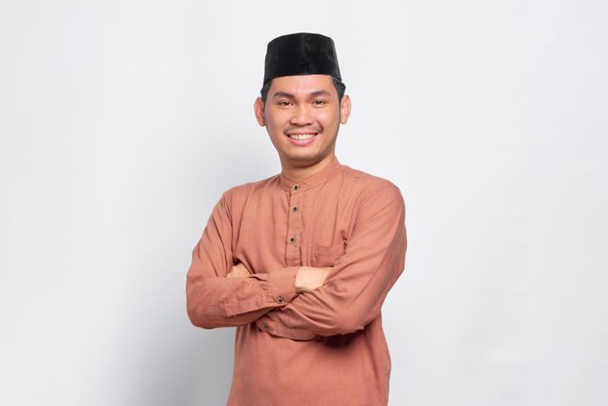 Muslim man in kufi head wear smiling with arms crossed