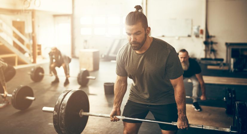 Focused man deadlifting heavy barbell in busy gym