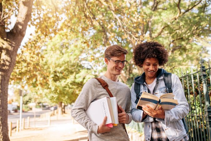 Two male students smiling and looking at textbook outdoors