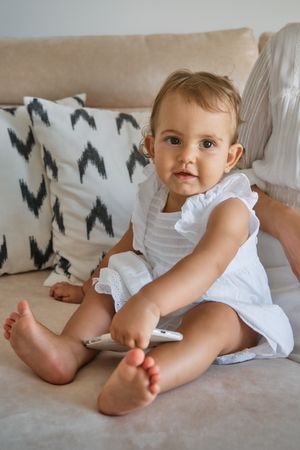 Cute little girl with smartphone sitting on bed