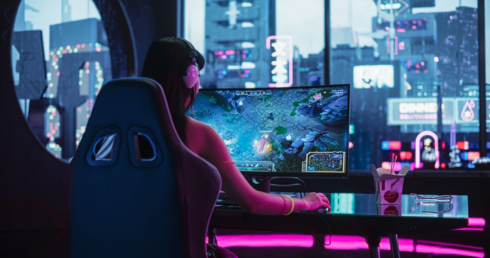 Young Woman Wearing Futuristic Clothes and Neon Rings, Playing Online Strategy Video Game on a Computer with Curved Monitor