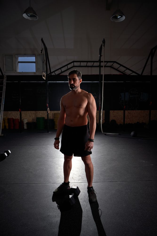 Shirtless sportsman standing in dark gym