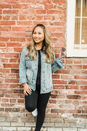 Woman in denim jacket leaning against red brick wall during daytime
