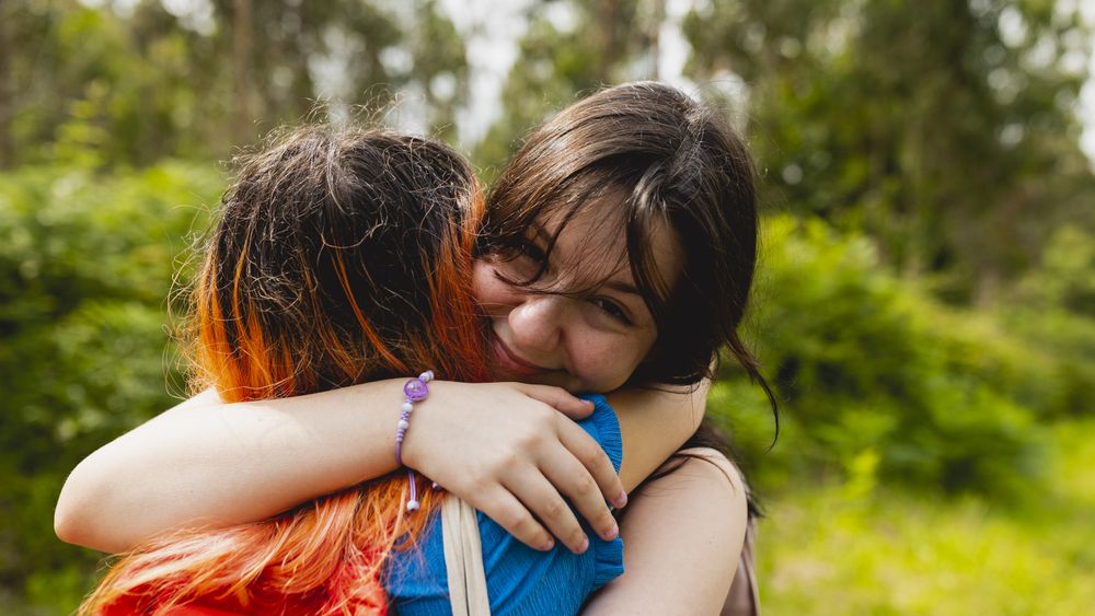 Two girlfriends, a couple, hug each other in love and happily during a walk in nature in the summer