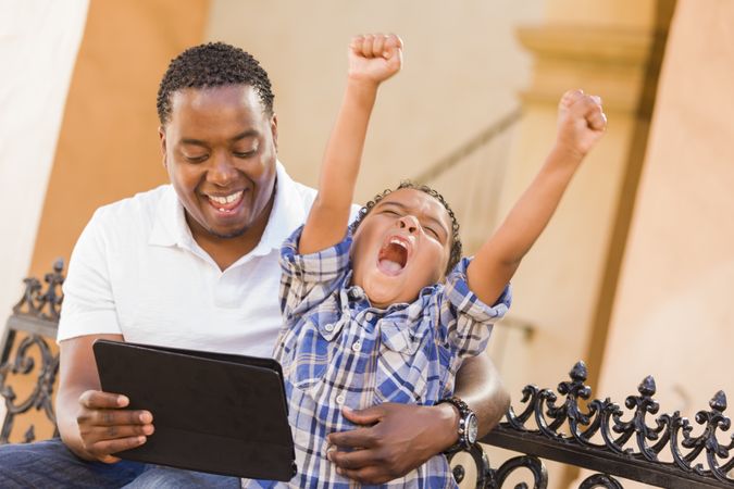 Black Father and Son Using Tablet On Balcony