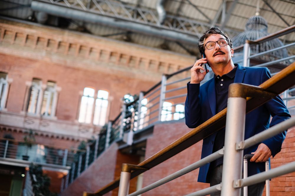Mature man standing with baggage and talking on smartphone