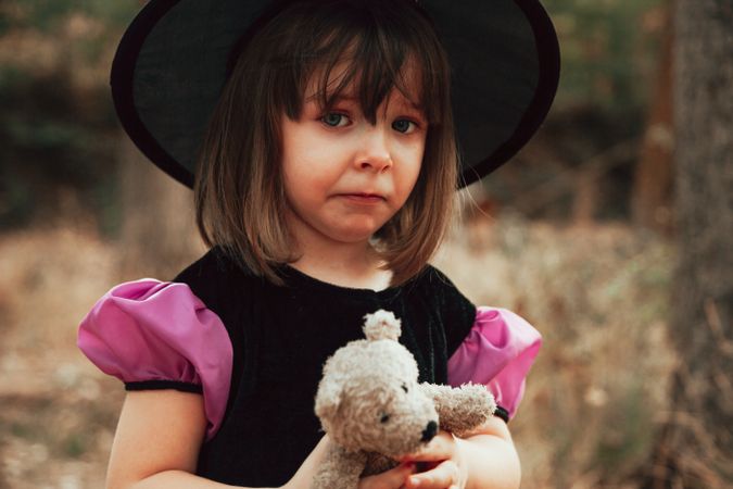 Portrait of sad girl in witch costume with her teddy bear