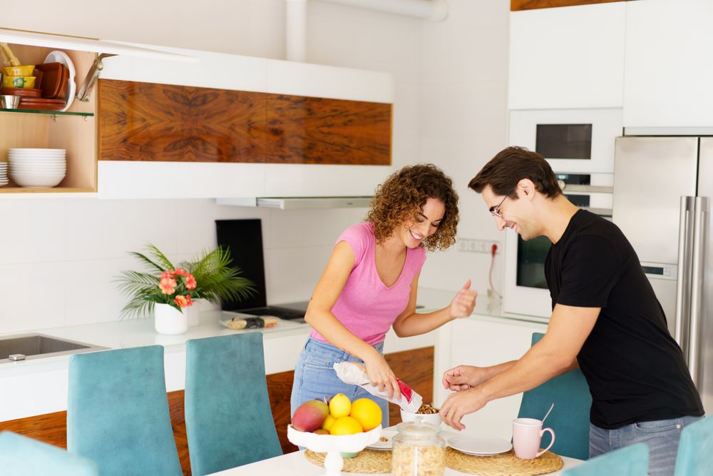 Happy adult couple standing near dining table and conversing in kitchen